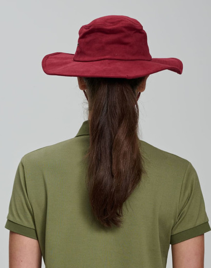 A maroon surf hat viewed from the back, worn by a person with long brown hair, paired with an olive green shirt.