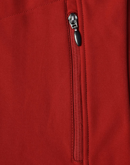 A close-up of a red softshell vest featuring a zippered pocket and a logo.