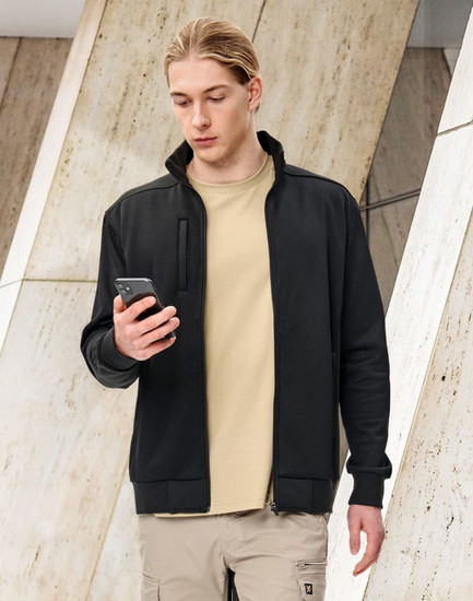 A man in a black fleece jacket holding a smartphone, set against a modern architectural background.