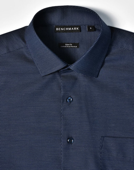 A navy blue button-up shirt featuring a pin dot pattern, with a single chest pocket and a branded label.