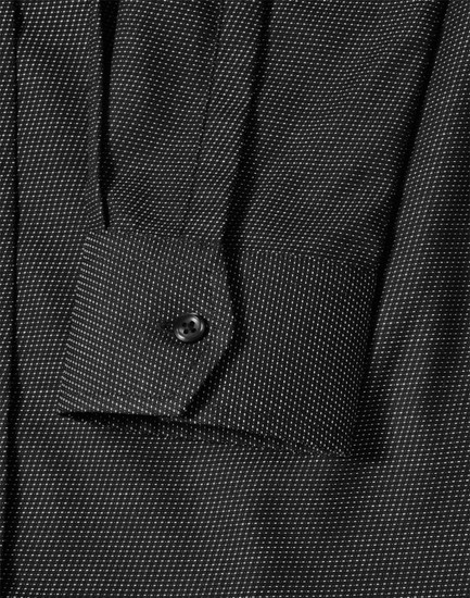 A close-up of a black pin dot stretch long sleeve shirt with a buttoned cuff and subtle pattern details.