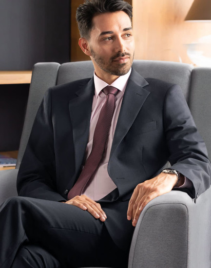 A men's two-button jacket in navy wool stretch, paired with a pink shirt and tie, displayed in a stylish setting.