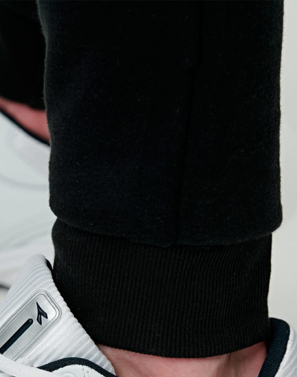 Black poly/cotton terry sweat pants with a fitted cuff, paired with sporty footwear.