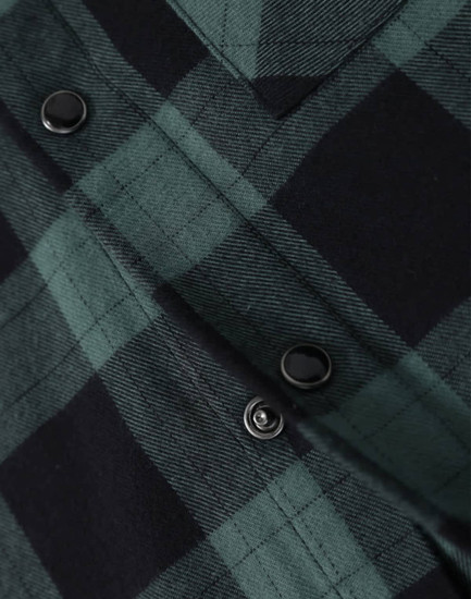 A close-up of a black and green flannel plaid shirt featuring button details. The shirt has a classic check pattern.