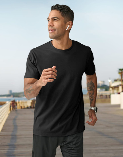 A man in a black short-sleeve tee shirt jogs along a seaside promenade, wearing earbuds and a watch.