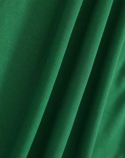 A close-up of green fabric with a textured surface, suitable for polo shirts. It features folds and a smooth appearance.