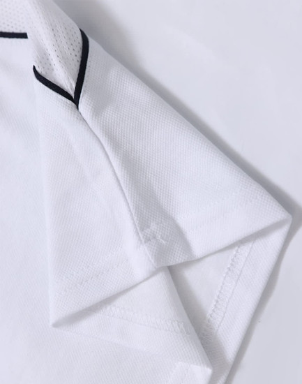 A white kids’ polo shirt with short sleeves and black detailing, featuring a logo.
