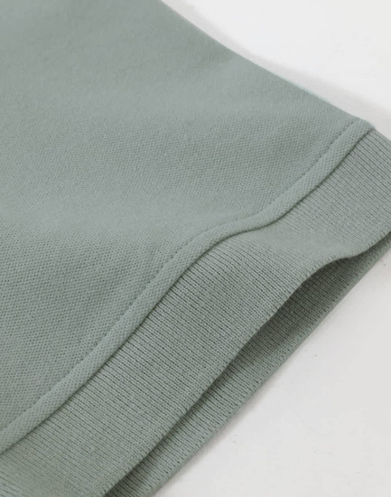 A close-up of the hem of a men's cotton stretch polo in a soft green colour, featuring a knitted cuff.