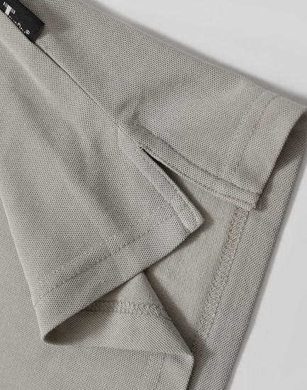 A light grey polo shirt featuring detailed stitching and a branded label at the collar.