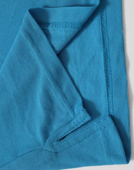 A close-up of a turquoise polo shirt featuring a fold at the sleeve and a branding logo.