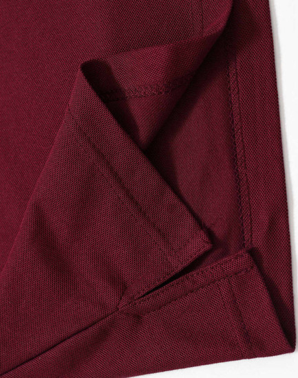 A close-up of the hem and fabric of a burgundy polo shirt, featuring a logo on one side.