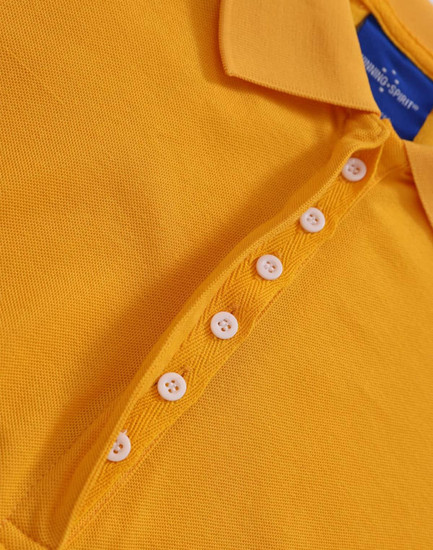 A close-up of a yellow polo shirt with a buttoned placket and a collar. The shirt features a logo.