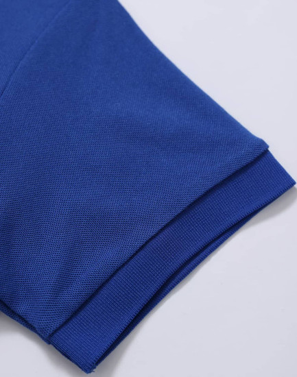 A close-up of a blue polo shirt featuring a textured fabric and rolled sleeves. The shirt has a logo.