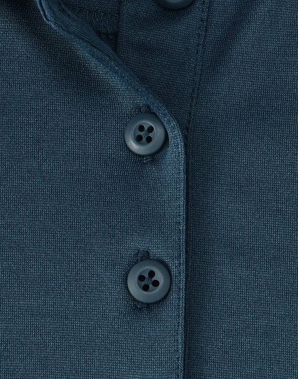 A close-up of a dark teal polo shirt featuring three buttons and a textured fabric. The shirt has a logo.