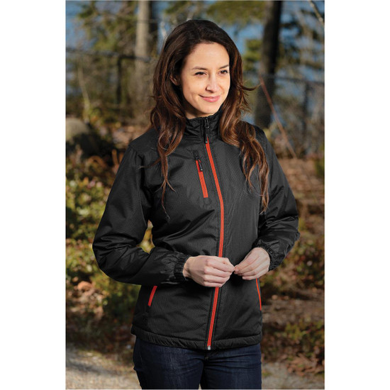 A woman wearing a black thermal jacket with red accents, standing outdoors in a natural setting. The jacket has a logo.