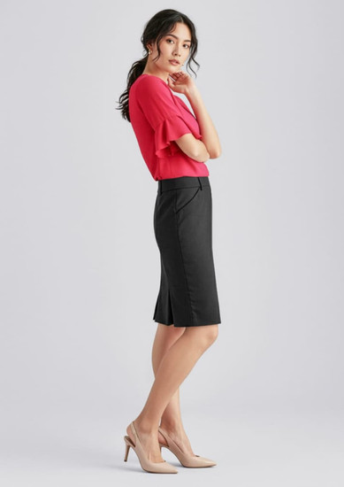 A woman in a red top and black wool stretch multi-pleat skirt stands elegantly, paired with nude heels.