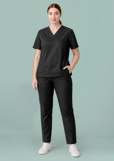 A woman is wearing a black scrub top with a V-neck and matching black pants, standing against a light green background.