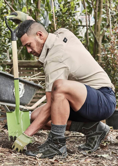 Men's lightweight outdoor shorts in navy, paired with a beige shirt, worn by a man kneeling with a shovel in a garden.