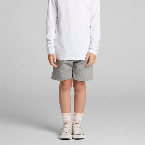 Kids stadium shorts in grey, featuring an elastic waistband and a logo, styled with a long-sleeve white top and sneakers.