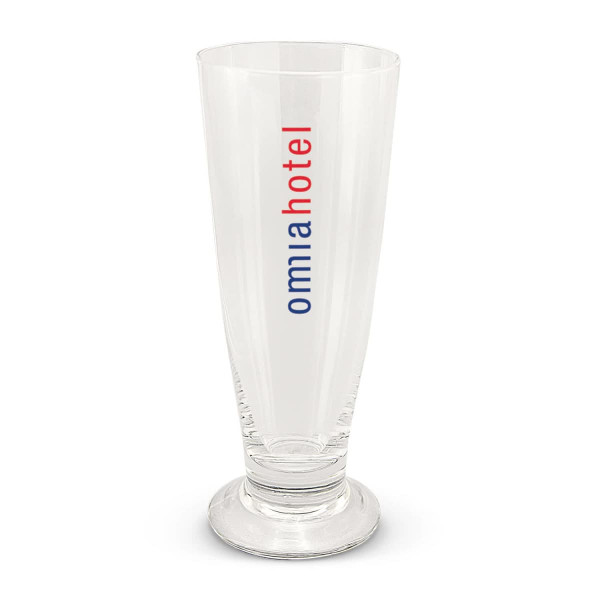 A clear beer glass with a tall, slender design and a base, featuring a logo in red and blue.