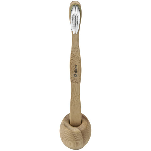A bamboo toothbrush in natural tan colour, with soft bristles, resting in a round holder. It features a logo.