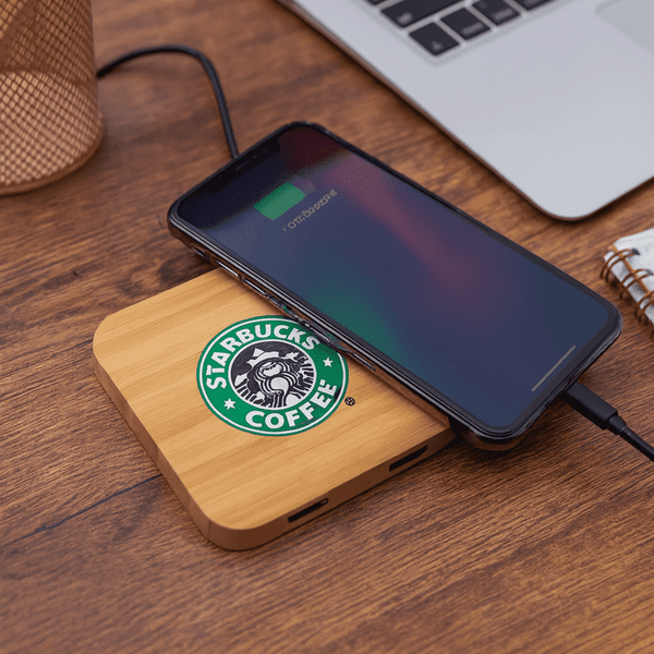 A bamboo wireless charging dock with a phone on top, featuring a logo and placed on a wooden surface.