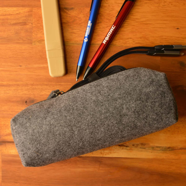 A gray felt utility case with a zipper, accompanied by pens and a highlighter placed on a wooden surface.