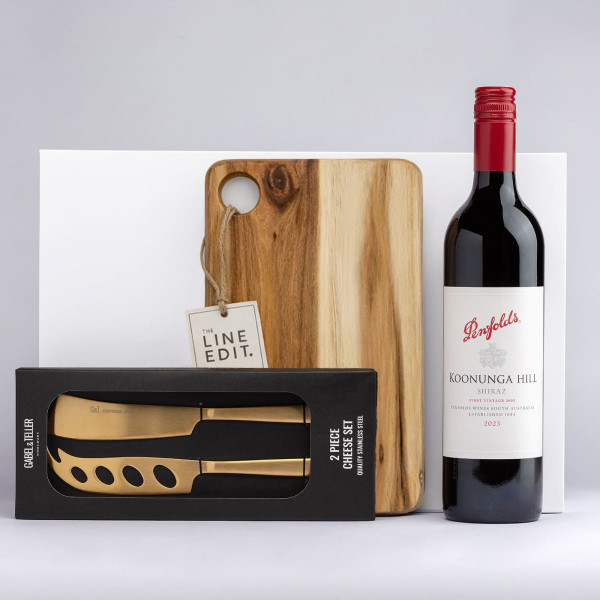 A wooden cheese board with a knife set in a box and a bottle of red wine. The board has a rounded cutout.