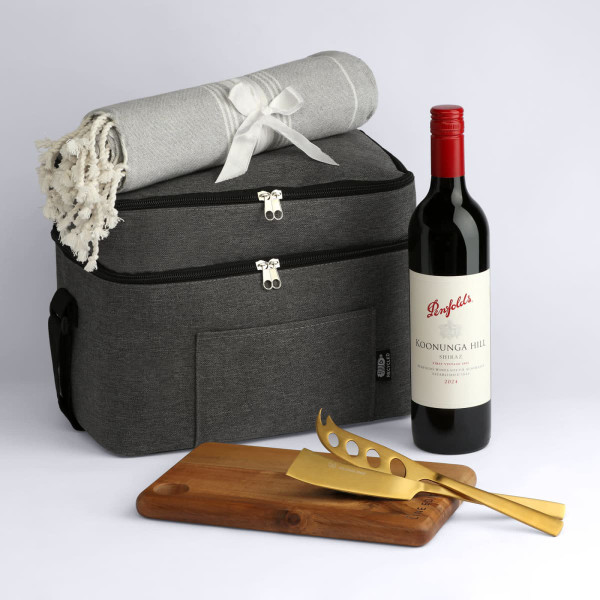 A cooler bag in grey with a blanket, a bottle of red wine, and wooden and gold utensils.