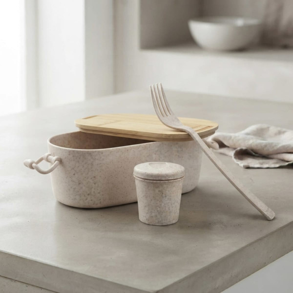 A bamboo lunch box in pale beige with a matching small container and a fork beside it, set on a concrete surface.