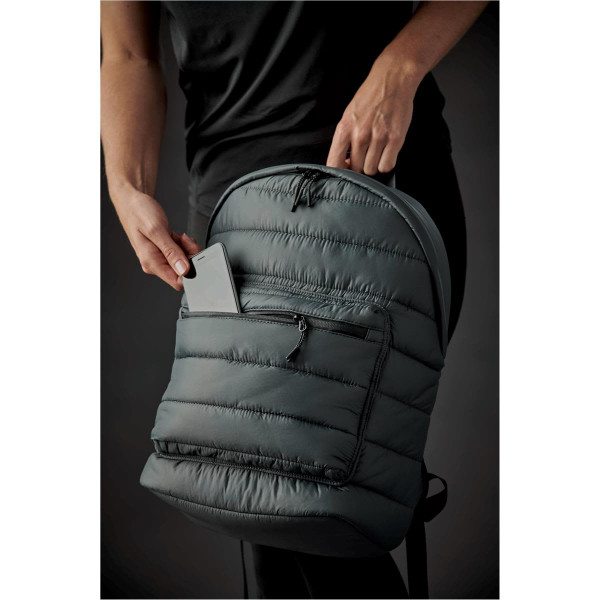 A quilted green backpack with a front pocket, being held by a person. The backpack has a logo on it.