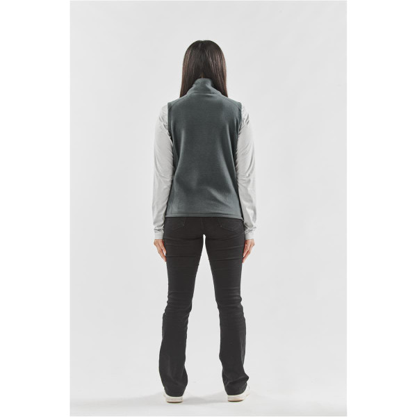 A woman stands with her back to the camera, wearing a grey fleece vest over a long-sleeved shirt, paired with black pants.