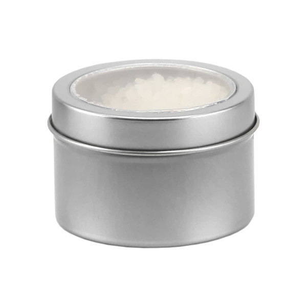 A silver tin containing white bath salts, featuring a clear lid. The tin has a smooth finish and a circular shape.