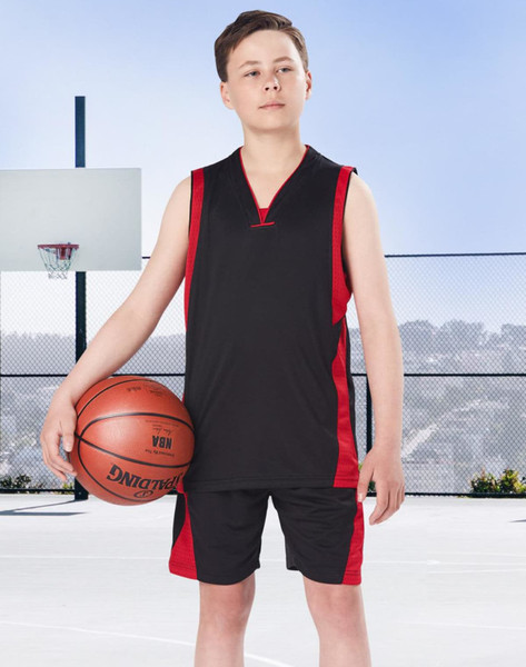 A young boy stands on a basketball court wearing black and red basketball shorts and a matching sleeveless top, holding a basketball.