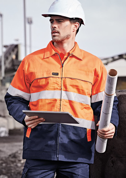 A man wearing a men's hi-vis cotton drill jacket in orange and navy, holding a blueprint and wearing a helmet.