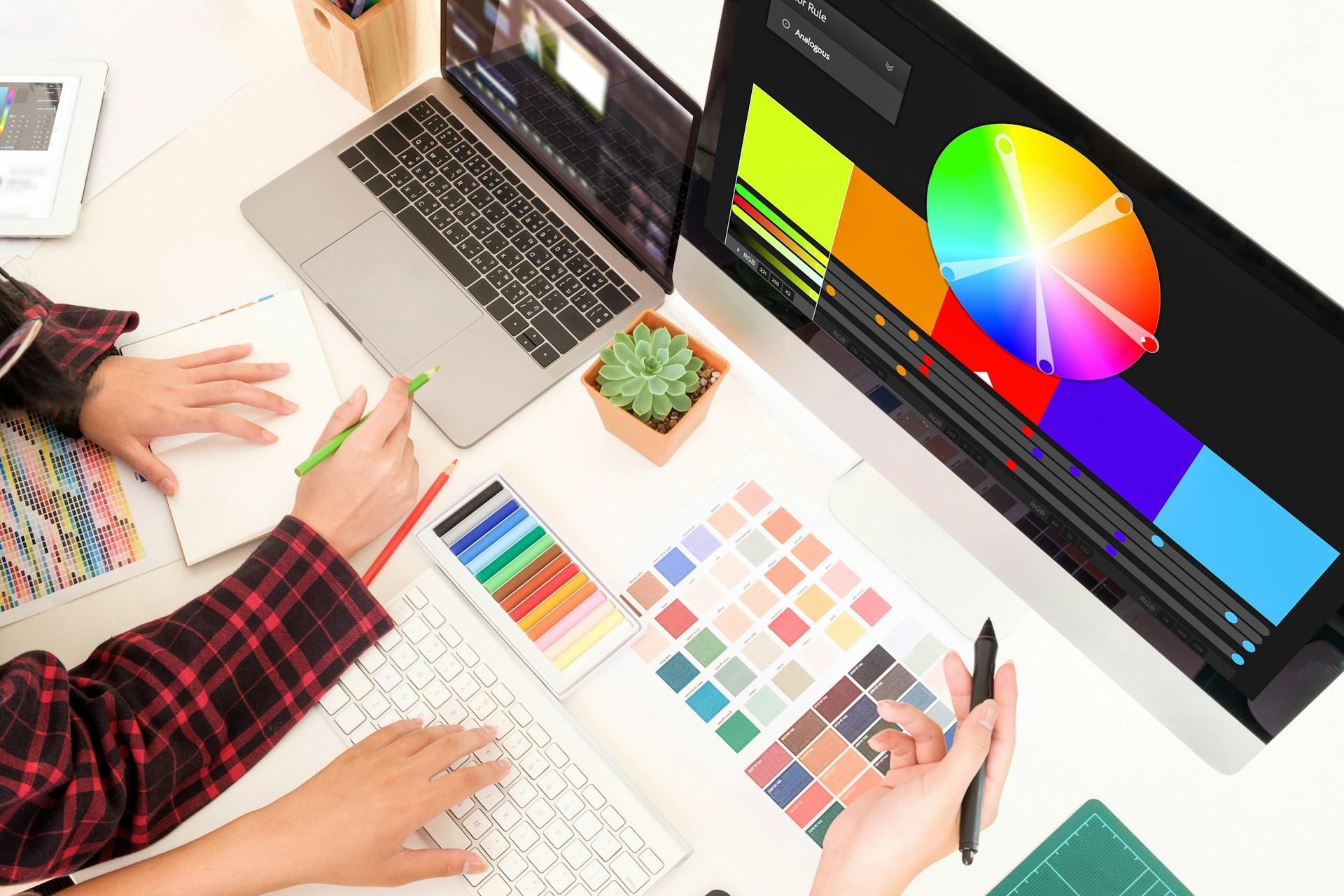 Designer choosing colours on a colour wheel on screen, with printed Pantone swatch books spread across the desk