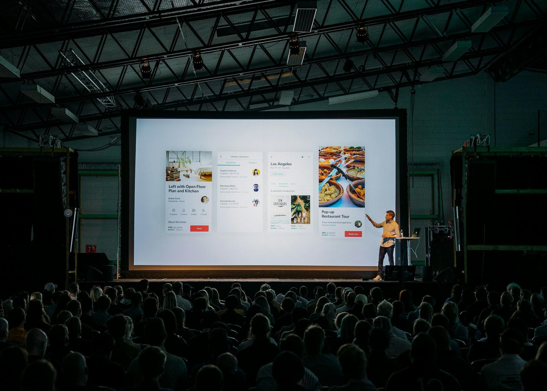 Speaker presenting app screens on a large stage at a tech conference