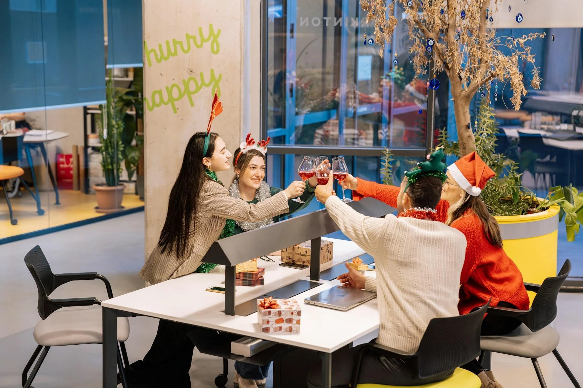 Four office employees "cheersing" their drinks over their office desk, Christmas decorations in the background