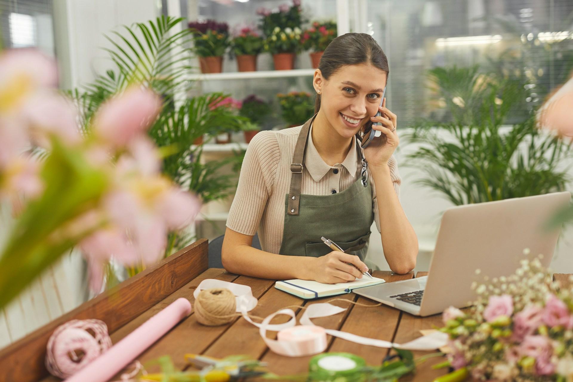 Small business florist taking an order by phone with a laptop and branded supplies