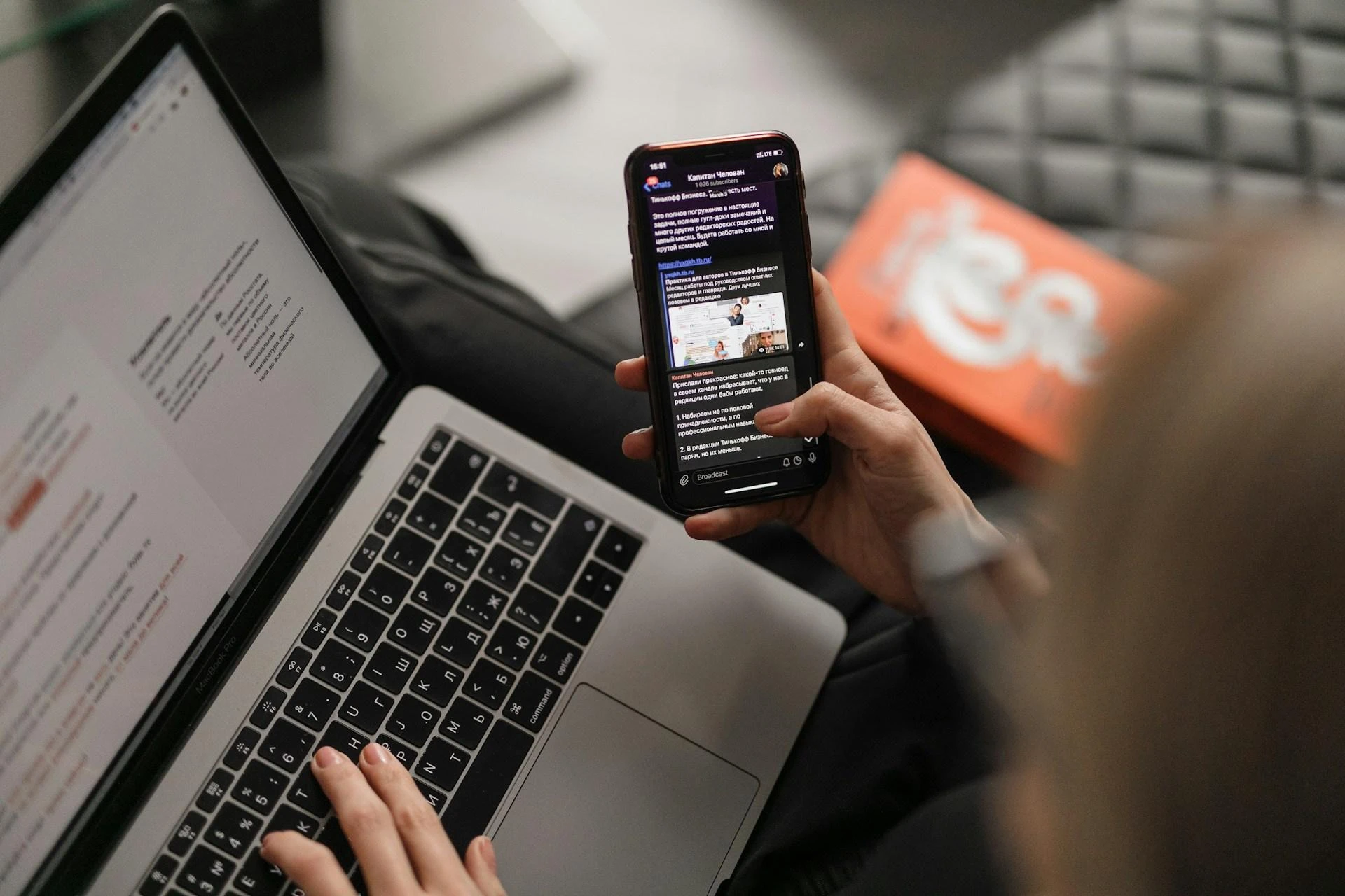 Person browsing social media on a phone while working on a laptop for event promotion