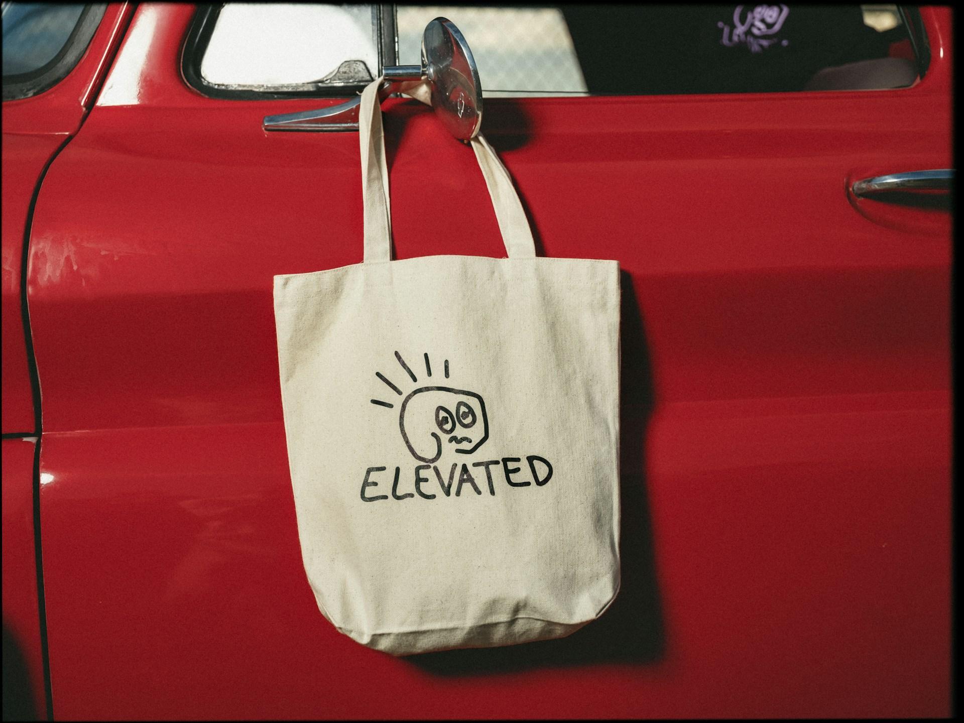Custom printed canvas tote bag hanging from a car door as a promotional giveaway