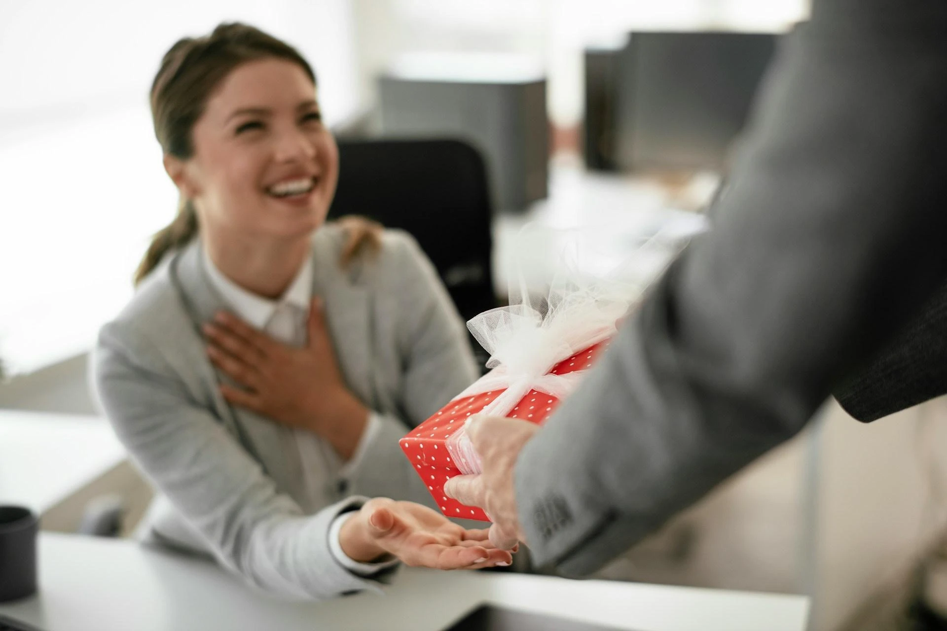 A woman holds her chest in appreciation at receiving a Christmas gift from her company