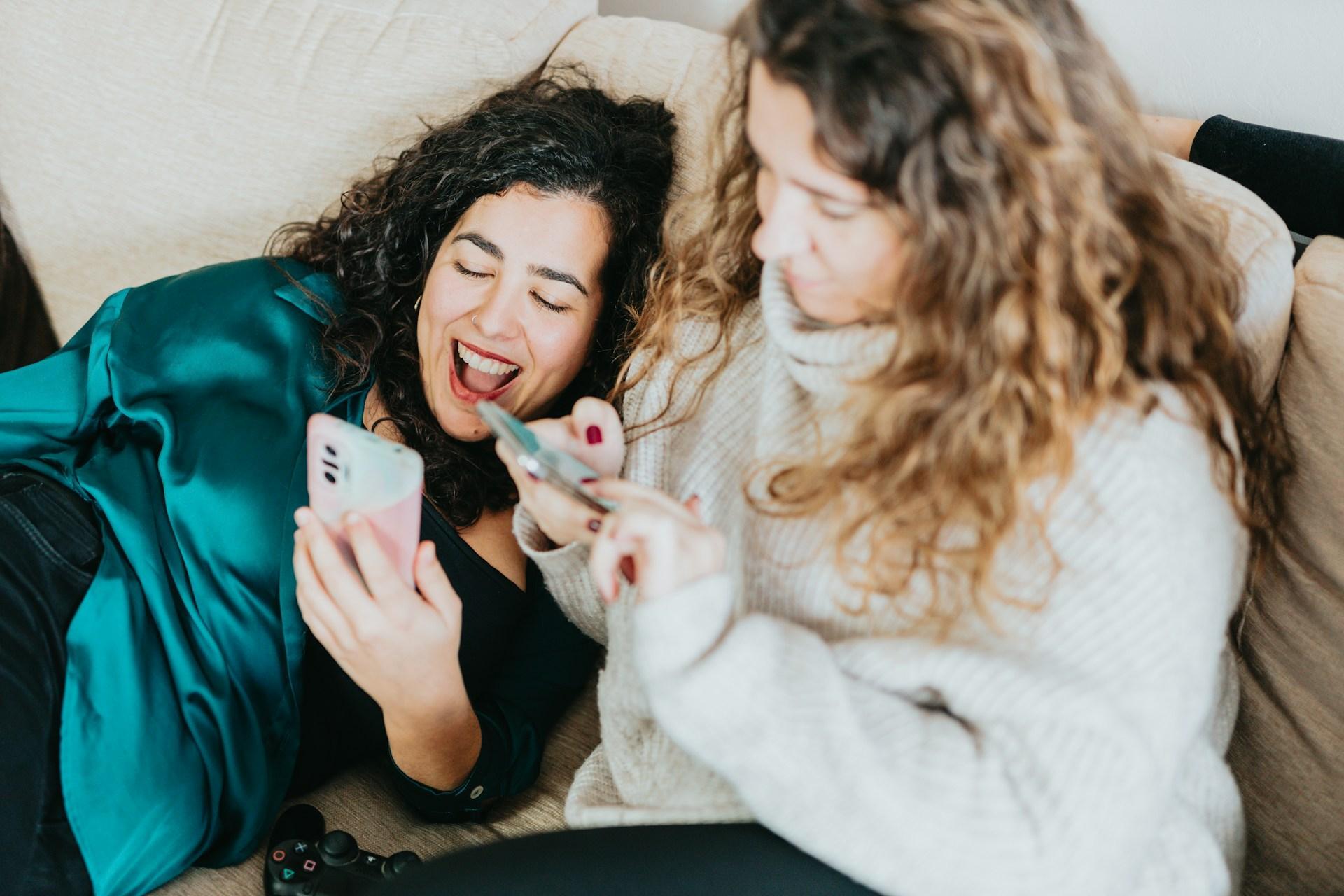 Two friends laughing while sharing event details on their phones