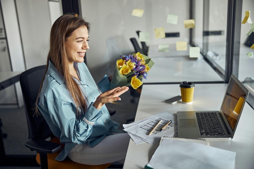 A woman in an office receives a bunch of yellow and purple flowers