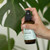 Mint Cleaning Linen & Room Spray | 125 ml - picture of hand spraying a bottle near a plant Mint Cleaning Linen & Room Spray | 125 ml - picture of hand spraying a bottle near a plant