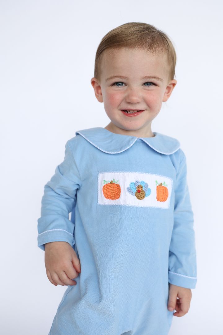 Smiling toddler boy wearing a light blue shirt with pumpkin and turkey applique, perfect for Thanksgiving.
