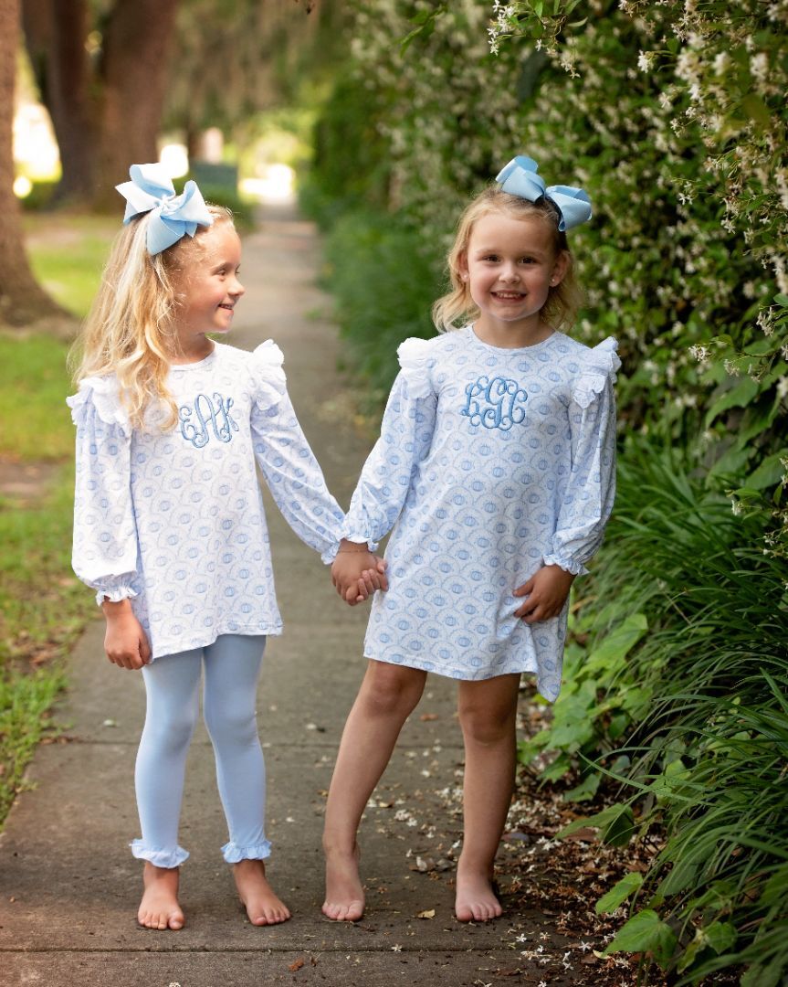 Two young girls holding hands, dressed in matching blue fall-themed outfits while walking outdoors.