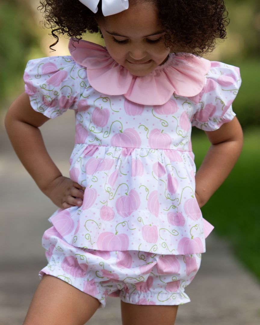 Little girl wearing a ruffled pastel dress with a leaf pattern, enjoying the fall weather.