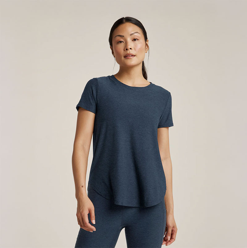 Beyond Yoga Women's Featherweight On The Down Low T-Shirt, a woman wearing a lightweight, dark blue casual T-shirt with a relaxed fit and short sleeves on a plain background.