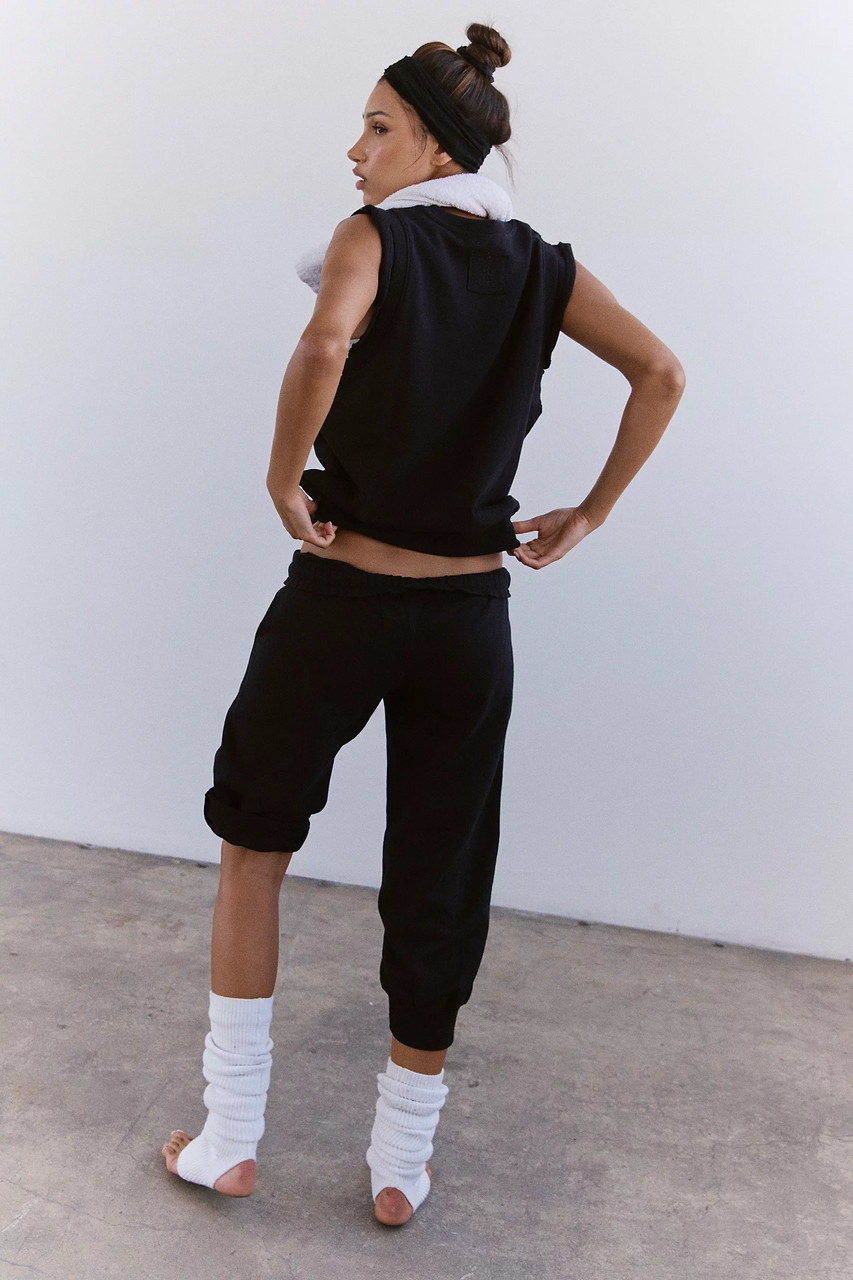 FP Movement Women's Flutter Tank, black sleeveless fitness top worn by a woman with a towel around her neck, paired with black jogger pants and white socks.